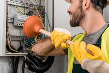 smiling electrician repairing electrical box with plunger in corridor