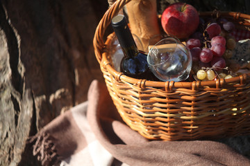 a picnic basket with  wine, cheese, grapes, apples outdoors