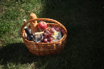 a picnic basket with  wine, cheese, grapes, apples outdoors