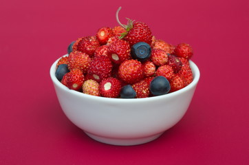 Porcelain bowl with strawberries and blueberries on crimson background