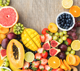 Top view of rainbow colored fruits, strawberries blueberries, mango orange, grapefruit, banana papaya apple, grapes, kiwis on the grey wood background, copy space for text, square, selective focus