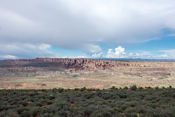 Vast desert landscape inside of Arches National Park. Clouds and blue sky with desert sagebrush in foreground