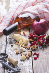 Rose wine bottle, fresh pomegranate, cheese, almond nuts on a wooden background.