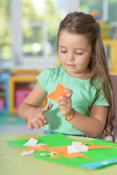 Cute llittle girl is cutting color paper