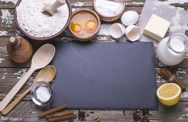 Fototapeta na wymiar Black board for recipe and the ingredients for baking homemade cookies - flour, butter, sugar, spices, lemon, milk on a wooden table. Flat lay