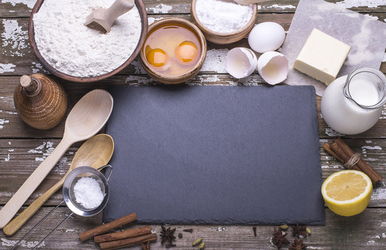 Black board for recipe and the ingredients for baking homemade cookies - flour, butter, sugar, spices, lemon, milk on a wooden table. Flat lay