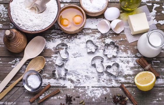 The cookie molds and ingredients for preparing Christmas homemade biscuits on a wooden table.