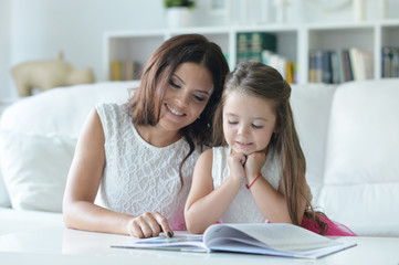 little cute girl reading book with mother at the table