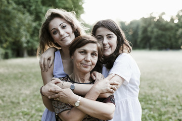 Mother and daughters embrace in a park at sunset on a summer evening