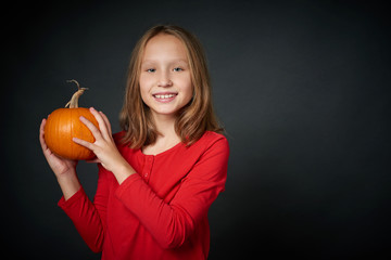 Smiling girl holding ripe pumpkin looking at camera, over dark background