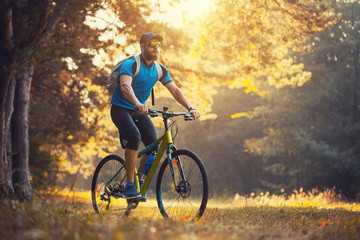 Fototapeta na wymiar Happy bearded man cyclist rides in the sunny forest on a mountain bike. Adventure travel.