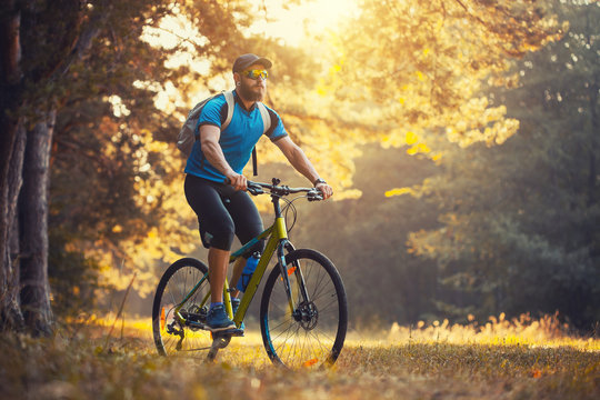 Happy Bearded Man Cyclist Rides In The Sunny Forest On A Mountain Bike. Adventure Travel.