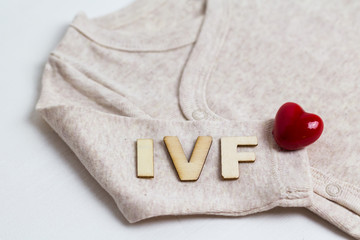 Baby clothes with wooden text IVF and heart. Concept - IVF, in vitro fertilization. Waiting for baby, pregnant