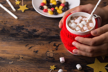 woman hands takes a mug of hot cacao with marshmallows knitted cloth for a mug christmas concept...