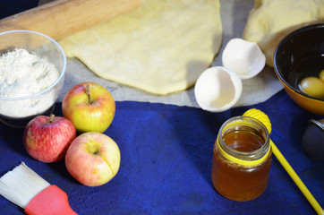 Various ingredients for winter seasonal baking and other recipes, honey, apples, herbs and spices on a dark blue background. Top view.