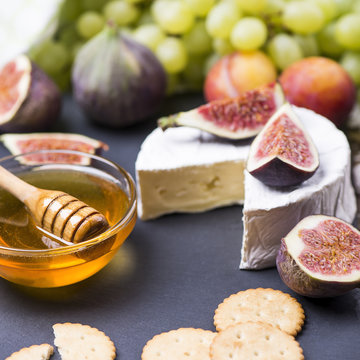 Soft cheese with fresh fruits - figs, grape, plums, honey, cookie cracker on a wooden background.