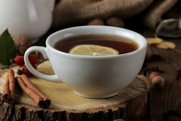 Autumn composition with hot tea on a wooden stand, cinnamon, dog rose, nuts on a brown wooden table