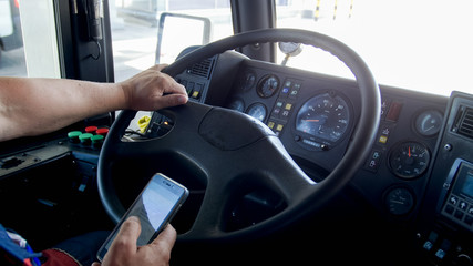 Closeup photo of bus driver using smartphone while driving. Danger in transport. Irresponsible...