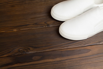 Fototapeta na wymiar White sneakers on dark brown wooden background. View from above, sneakers in the corner