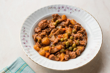 Turkish traditional tas kebab with potato, pea and tomato in a white plate
