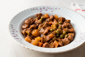 Turkish traditional tas kebab with potato, pea and tomato in a white plate