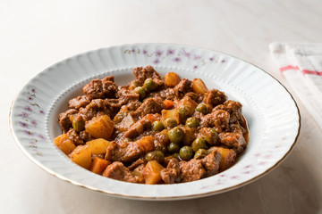 Turkish traditional tas kebab with potato, pea and tomato in a white plate
