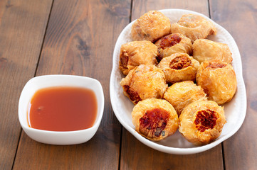 Deep fried crap meat roll and sweet chill sauce on white dish on wooden table.Thai food and selective focus.
