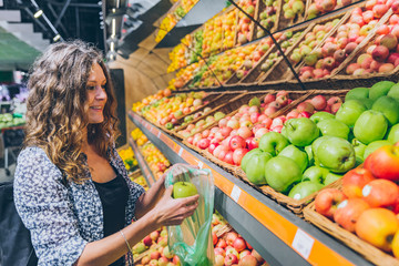 young adult woman choosing apples in grocery store