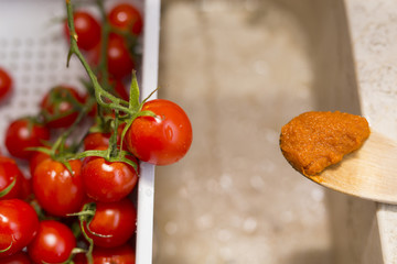 image of cherry tomatoes in plastic container and wooden spoon with tomato sauce