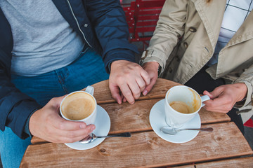 couple holding hands while drinking latte in outdoors cafe