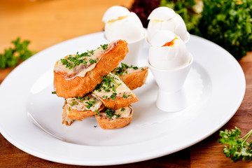 Sliced bread with cream cheese and soft boiled eggs on white plate. Close up