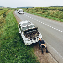 man sitting on road near broken car. trying stop car for help