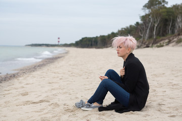 Fototapeta na wymiar beautiful lonely sad girl hipster with a stylish hairstyle and pink hair smokes and looks at the sea