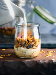 Homemade granola with honey, raisins, cherries, sesame and chestnuts in a glass on wooden board....
