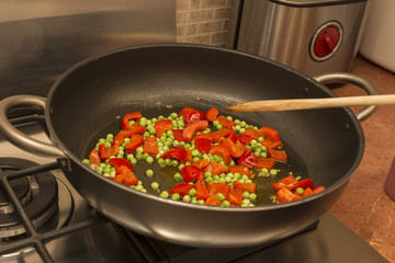 horizontal image of a pan for the preparation of paella with peas and tomatoes inside.