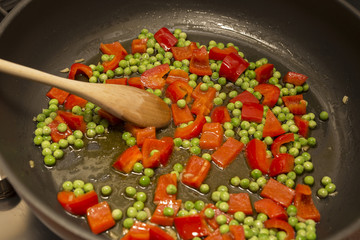 horizontal image of a pan for the preparation of paella with peas and tomatoes inside.