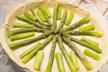 horizontal image with a top view of a savory pie with green asparagus during its preparation