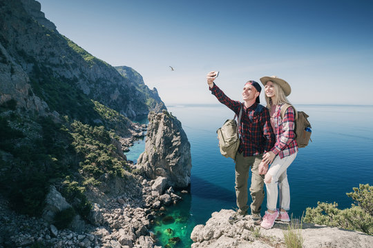 Young couple hikers taking selfie photo on phone in the mountains background the sea. Beautiful Man and Woman traveling active adventure vacations.