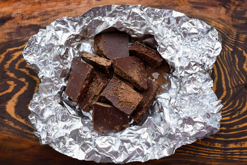 Pieces of chocolate on foil on dark wooden background