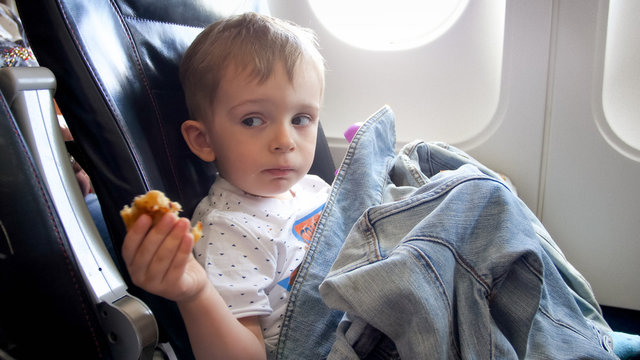 Portrait of 2 years old toddler boy having snack during flight in airplane