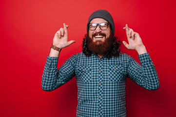 Naklejka premium Portrait of bearded man with crossed fingers over red background