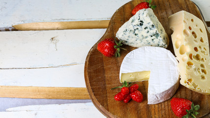 Cheese Assortment Board: Camembert or Brie, Dourble, Maasdam and strawberry in rural wooden surface. Authentic lifestyle image. Top view. Copy space