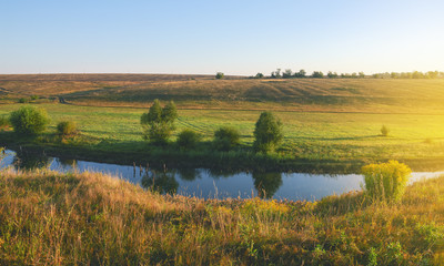 Zonnig zomerlandschap met rivier die stroomt tussen de prachtige groene heuvels, velden en weiden.