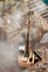 Building demolition with an excavator in dust cloud, view from above.