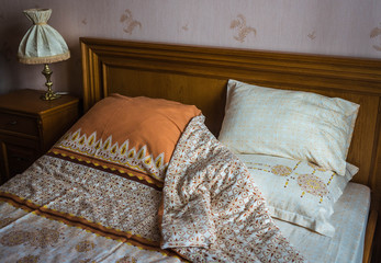 Beautifull linens, pillows and blankets on brown wooden bed and bed-side lamp