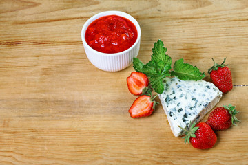 cheese dourble or brie with blue mildew with strawberry jam and mint on a wooden background. Top view. Copy space