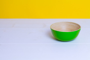 Bamboo green plate on white wooden table, yellow color paper background, paper pattern, side view