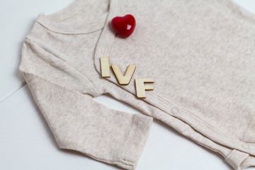 Baby clothes with wooden text IVF and heart. Concept - IVF, in vitro fertilization. Waiting for baby, pregnant - 225381236