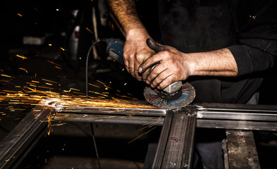 Craftsman sawing metal with disk grinder in workshop. Grinding metal with sparks flying.