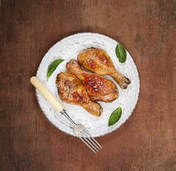 Roasted chicken drumsticks with sesame on a plate on a wooden background